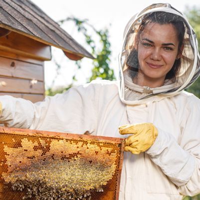 Young female beekeeper hold wooden frame with honeycomb. Collect honey. Beekeeping concept